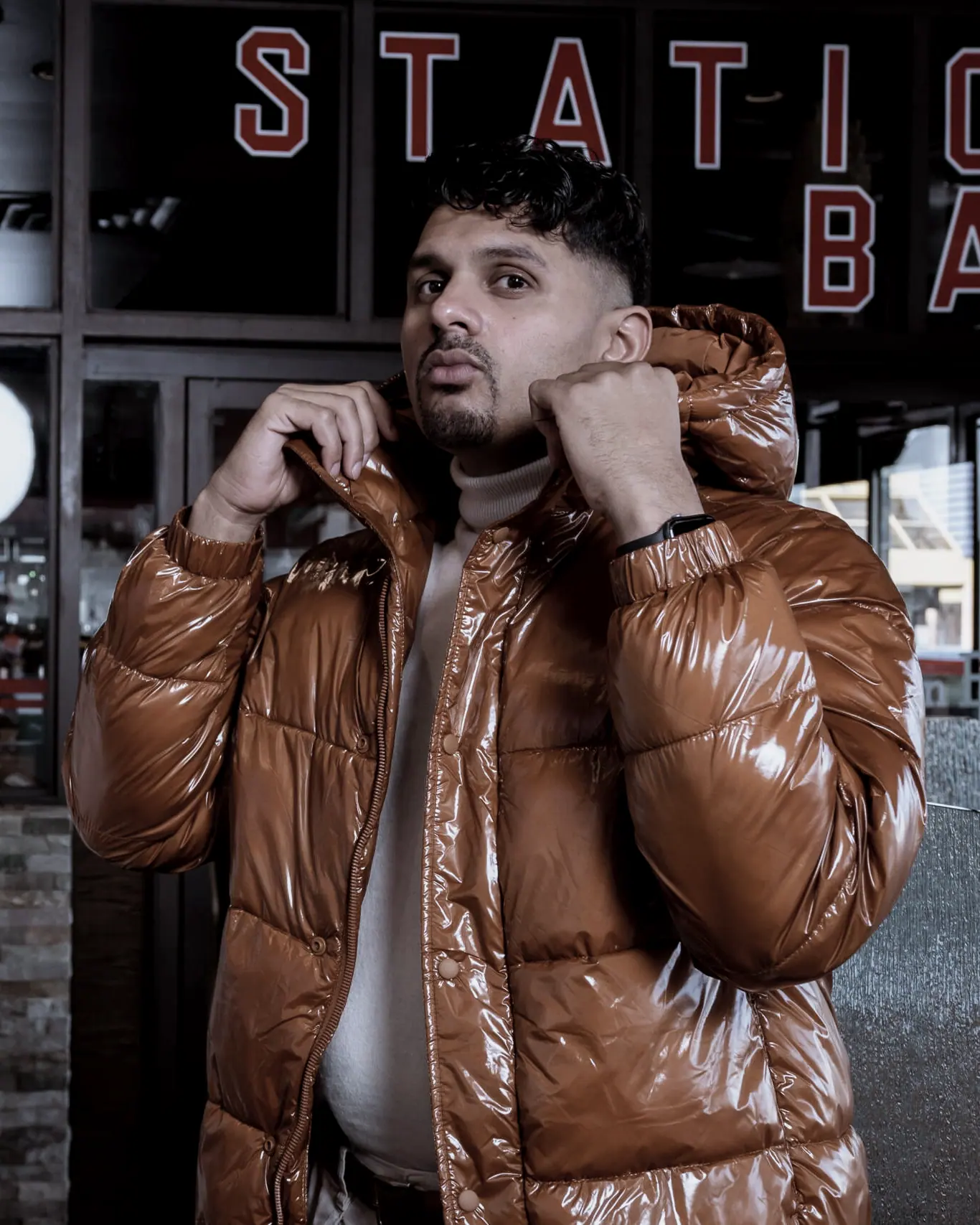 One of the leads outside a bar in a brown puffer jacket, a neon sign behind him.
